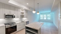 Located at 10520 Lakeline Mall Dr in Austin, TX, this well-appointed one-bedroom, one-bathroom residence offers a thoughtfully designed single-floor layout. The open-concept kitchen and living area serves as the heart of the home, featuring a large granite-topped island with a teal accent base, elegant pendant lighting, and crisp white subway tile backsplash. Gray shaker-style cabinetry lines the walls, complemented by stainless steel appliances including a gas range, built-in microwave, refrigerator, and dishwasher. Open shelving and built-in cabinetry provide generous storage throughout. Light hardwood flooring flows seamlessly across the entire space, enhancing the bright and airy atmosphere created by recessed lighting and large windows. The spacious living area receives ample natural light and features direct outdoor access through a side door. The generously sized primary bedroom includes a ceiling fan, a built-in granite-top desk with cabinetry, and large windows with views to the outside. The bathroom is finished with large-format tile flooring, a granite dual-sink vanity with gray cabinetry, a tub-shower combination with striped tile surround, and stylish sconce lighting. A dedicated entrance and closet complete this clean, modern residence.