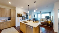 This well-designed single-floor residence offers a thoughtfully planned open-concept layout that seamlessly connects the kitchen, dining, and living areas. The kitchen is a standout feature, showcasing flat-front light wood cabinetry, a suite of stainless steel appliances including a side-by-side refrigerator, range, and built-in microwave, and a central island with a quartz countertop, undermount sink, and pendant lighting overhead. Rich hardwood-style flooring runs throughout the main living areas, adding warmth and continuity to the space. The living room benefits from abundant natural light through large windows and a glass door that opens to the outdoors, offering views of the surrounding area. Two bedrooms provide comfortable retreats, each featuring plush carpeting, ceiling fans, and windows that invite natural light. Both bathrooms mirror the home's modern aesthetic with light wood vanities, white quartz countertops, large wall mirrors with integrated lighting, and clean white tile work. One bathroom includes a tub-shower combination, while the other features access to a walk-in closet. Throughout the residence, crisp white walls and consistent design elements create a cohesive, contemporary ambiance that is both functional and inviting.