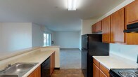 Located at 16102 East Broadway Avenue in Spokane Valley, WA, this single-floor unit offers a practical and comfortable layout with consistent finishes throughout. The kitchen is well-appointed with warm honey-toned wood cabinetry, light countertops, hardwood-style flooring, black appliances including a refrigerator, dishwasher, and electric range, and ample upper and lower cabinet storage arranged in a galley-style configuration. The kitchen opens toward a generously sized living area carpeted in neutral tones, featuring a sliding glass door that provides access to a private patio and fills the space with natural light. A wall-mounted HVAC unit is also present in the living area. The bedrooms are carpeted and bright, with large windows that bring in natural light and offer views of the surrounding neighborhood. The unit includes two bathrooms, each featuring wood-toned vanity cabinetry, light countertops, and hardwood-style flooring. One bathroom includes a full tub-shower combination, while the other is finished with a vanity, mirror, and stylish light fixture above. Throughout the unit, clean white walls, wood trim baseboards, and consistent flooring materials create a cohesive and move-in-ready aesthetic suited for comfortable everyday living.