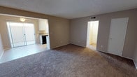 This single-floor residence offers a practical and comfortable layout across several well-defined living spaces. The main living area is generously sized, featuring neutral-toned carpet underfoot, warm beige walls, and a textured ceiling. A front entry door opens directly into this inviting space, which connects seamlessly to the rest of the home. Large windows dressed with vertical blinds allow natural light to fill the rooms, creating a bright and airy atmosphere throughout.

The bedroom areas are spacious and similarly finished with plush carpet and warm neutral walls, each benefiting from natural light through sizable windows. One bedroom includes an additional door, likely to a closet, providing convenient storage. The rooms are well-ventilated with ceiling vents ensuring comfortable airflow.

The galley-style kitchen is efficiently arranged, featuring white cabinetry on both sides, granite-style countertops, a double stainless steel sink, and black appliances including a gas range and dishwasher. Tile flooring and overhead lighting make this a clean, functional workspace.

The bathroom is thoughtfully designed with a granite-style vanity countertop, white cabinetry, a large mirror, and brushed nickel fixtures. A separate water closet area houses the shower-tub combination and toilet, finished with tile flooring for easy maintenance. Overall, the space presents a clean, move-in ready environment with consistent finishes throughout.