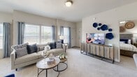 This thoughtfully designed single-floor residence offers a practical and comfortable layout across four bedrooms, a combined living and dining area, a full kitchen, and a connecting hallway. The kitchen is a standout feature, showcasing white cabinetry with sleek hardware, dark stone countertops, a subway tile backsplash, stainless steel appliances including a French door refrigerator and electric range, and wood-look tile flooring that adds warmth underfoot. A peninsula with a sink provides additional prep space and casual seating. The open living and dining area is bright and inviting, with large windows dressed in light curtains that allow natural light to fill the carpeted space. The dining area accommodates a round table and chairs, while the living room offers generous room for seating and entertainment. The primary bedroom is a comfortable retreat featuring plush carpet, natural light from a window, and a spacious walk-in closet with built-in wire shelving. Additional bedrooms are equally well-sized, each with carpet flooring, ceiling fans, and windows. The bathroom features wood-look tile flooring, a dark stone vanity top, white cabinetry, and a shower-tub combination. Throughout the residence, neutral tones and consistent finishes create a cohesive, modern aesthetic.