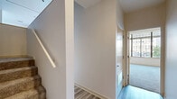 This single-floor, 1-bedroom, 2-bathroom urban residence offers a thoughtfully designed layout with clean, modern finishes throughout. The living area features light-toned hardwood-style flooring and large floor-to-ceiling windows framed in dark trim, allowing an abundance of natural light while showcasing dynamic city views of the surrounding downtown streetscape and architecture. Track lighting accents the open living space, adding a contemporary touch.

The generously sized primary bedroom is carpeted for comfort and is lined with expansive windows that provide sweeping urban views, creating a bright and airy atmosphere. A dedicated closet offers practical storage.

Both bathrooms are finished in a clean, neutral palette with tiled flooring, full tub-shower combinations, and warm wood-toned vanities with countertop sinks. One bathroom conveniently houses a stacked in-unit washer and dryer, eliminating the need for shared laundry facilities.

A hallway connects the various spaces efficiently, with light wood-style flooring and a staircase with a sleek handrail visible from the entry. Warm beige walls and white trim run consistently throughout, lending the residence a cohesive and polished feel. This well-lit urban home is ideal for those seeking modern city living with functional, comfortable interiors.