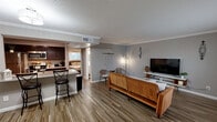 Located at 7400 Jones Drive in Galveston, TX, this well-appointed one-bedroom, one-bathroom unit offers a thoughtfully designed single-floor layout that maximizes its comfortable footprint. Wood-look plank flooring runs throughout, tying the open-concept living spaces together seamlessly.

The living room is bright and inviting, featuring crown molding, a large window dressed with sheer curtains that invite natural light, and decorative wall accents that add character to the neutral gray palette. It flows directly into the combined kitchen and dining area, where dark cabinetry, a tiled mosaic backsplash, and a generous granite-topped peninsula with bar seating create a functional and stylish hub for cooking and entertaining. Track lighting and pendant fixtures illuminate the space, and a stainless steel refrigerator completes the kitchen.

The bedroom is spacious and tranquil, finished with the same wood-look flooring and a ceiling fan with light fixture. A dedicated walk-in closet provides ample storage, and the room offers easy access to the full bathroom. The bathroom features a white shaker-style vanity, wood-look tile flooring, and a tiled walk-in shower with a glass enclosure and a classic hexagonal tile surround. A dedicated laundry area rounds out the unit's practical amenities.