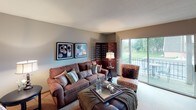 This thoughtfully designed single-floor residence offers a cohesive and inviting atmosphere throughout its key living spaces. The living room serves as the heart of the home, featuring soft neutral gray walls, plush carpeting, and large sliding glass doors that flood the room with natural light and provide views of a lush outdoor setting. A decorative room divider, framed wall art, and a mix of comfortable seating create a warm and welcoming ambiance.

The galley-style kitchen is efficiently laid out with warm oak cabinetry, granite-look countertops, and tile flooring. Black appliances — including a range, microwave, refrigerator, and dishwasher — anchor the space and offer a sleek contrast to the cabinetry's natural tones.

The bedroom is a serene retreat, highlighted by a rich taupe accent wall, soft carpeting, and a large window that brings in natural light. Matching nightstands with warm-toned lamps flank the bed, and a wood-paneled closet door adds a classic touch. The room carries an elegant, restful quality well-suited for relaxation.

The bathroom is clean and classic, featuring tile wainscoting, a vanity with a wood-framed mirror, and a tub-shower combination. Neutral tones throughout maintain a calm, spa-like feel. Together, these spaces form a harmonious and functional home with consistent, tasteful design choices.