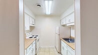 This single-floor residential unit offers a clean, functional layout designed for comfortable everyday living. The galley-style kitchen is efficiently arranged with white cabinetry lining both walls, providing ample storage space. Light wood-toned countertops complement the all-white appliances, including a coil-burner electric range and a top-freezer refrigerator. Overhead fluorescent lighting and light tile flooring complete the practical kitchen design.

The living area is generously proportioned, featuring warm neutral carpet and a textured ceiling. A sliding glass door opens directly to a private balcony, allowing natural light to flow into the room and offering a pleasant outdoor view of surrounding greenery. A hallway connects the living space to the rest of the unit, maintaining a logical and open flow throughout.

The bedroom is a comfortable, carpeted room with a window that frames a leafy outdoor view, filling the space with natural light. A reach-in closet provides convenient built-in storage.

The bathroom is straightforward and well-maintained, featuring a full-size soaking tub with an overhead shower, chrome fixtures, and clean white finishes. The overall aesthetic of the unit is neutral and move-in ready, with light-toned walls and soft carpeting creating a calm, livable atmosphere throughout.