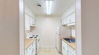 This single-floor residential unit offers a clean, functional layout designed for comfortable everyday living. The galley-style kitchen is efficiently arranged with white cabinetry lining both walls, providing ample storage space. Light wood-toned countertops complement the all-white appliances, including a coil-burner electric range and a top-freezer refrigerator. Overhead fluorescent lighting and light tile flooring complete the practical kitchen design.

The living area is generously proportioned, featuring warm neutral carpet and a textured ceiling. A sliding glass door opens directly to a private balcony, allowing natural light to flow into the room and offering a pleasant outdoor view of surrounding greenery. A hallway connects the living space to the rest of the unit, maintaining a logical and open flow throughout.

The bedroom is a comfortable, carpeted room with a window that frames a leafy outdoor view, filling the space with natural light. A reach-in closet provides convenient built-in storage.

The bathroom is straightforward and well-maintained, featuring a full-size soaking tub with an overhead shower, chrome fixtures, and clean white finishes. The overall aesthetic of the unit is neutral and move-in ready, with light-toned walls and soft carpeting creating a calm, livable atmosphere throughout.