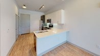 This single-floor unit offers a thoughtfully designed open-concept layout that seamlessly connects the kitchen, dining, and living areas. The kitchen is a standout feature, showcasing two-tone cabinetry with white upper cabinets and charcoal lower cabinets, a marble-patterned tile backsplash, stainless steel appliances including a range, microwave, dishwasher, and refrigerator, and a peninsula with a light quartz countertop and undermount sink — ideal for both meal preparation and casual dining. Light wood-style flooring runs throughout the main living areas, adding warmth and continuity to the space. The bedroom is generously sized, featuring plush carpet, multiple windows with horizontal blinds that allow for abundant natural light, and sliding glass doors that open to an outdoor view of lush greenery. The bathroom is elegantly finished with a long vanity topped with white quartz, charcoal cabinetry with brushed nickel hardware, a large mirror with modern lighting, and a full tub and shower combination finished with large-format gray tile. Track lighting and recessed ceiling fixtures provide versatile illumination throughout. The overall design is clean and contemporary, with a neutral color palette that creates a bright, cohesive atmosphere throughout the unit.