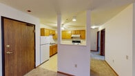 This single-floor residence offers a practical and comfortable layout designed for everyday living. The spacious living area is carpeted and filled with natural light from large windows, and is accented by an elegant chandelier that adds a warm, inviting glow. A seated nook near the window provides a cozy retreat with views of the surrounding outdoors.

The kitchen is well-equipped and thoughtfully designed, featuring light maple cabinetry, generous counter space, and white appliances including a range, dishwasher, and refrigerator. A ceiling fan overhead keeps the space comfortable, while a peninsula with a breakfast bar connects the kitchen to the main living area, enhancing the open-concept flow. Tile flooring in the kitchen provides a clean contrast to the carpeted living spaces.

The bedrooms are quiet and comfortable, each carpeted and featuring natural light from exterior windows with blinds. One bedroom includes a substantial double-door closet with warm wood-toned paneling, offering excellent storage capacity.

The bathroom is clean and functional, appointed with light maple cabinetry, a single vanity with a mirror, tile flooring, and a full tub-shower combination with a curtain surround and grab bar for added safety. The overall palette throughout the residence is neutral and bright, creating a welcoming and move-in-ready environment.