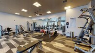 The fitness center at Encore, located at 470–498 E 400 S in Salt Lake City, Utah, is a thoughtfully designed single-floor facility offering a comprehensive workout environment. The space is defined by its striking geometric-patterned luxury vinyl flooring, which combines tones of beige, gray, and dark brown to create a visually dynamic foundation throughout the room.

Natural light plays a prominent role in the space, with floor-to-ceiling windows along one wall providing outdoor views of the surrounding streetscape and mature trees, lending an open and energizing atmosphere. Recessed and flush-mounted ceiling light panels supplement the natural light, ensuring the space remains bright and well-illuminated throughout the day. A ceiling fan adds to the comfort of the workout environment.

Full-wall mirrors are strategically positioned to visually expand the space and allow users to monitor their form during exercise. The cardio zone features multiple treadmills, elliptical trainers, and stationary bikes, all positioned to take advantage of the exterior views. The strength training area includes cable machines, multi-function weight stations, a dumbbell rack with a full range of free weights, a weight bench, and rubber mat flooring for protection and safety. Wall-mounted flat-screen televisions provide entertainment, and frosted glass doors offer a polished, contemporary entrance to the facility.