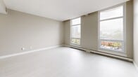 Located at 450 Rue Sherbrooke E in Montréal, this efficiently designed unit offers a well-organized single-floor layout comprising a bedroom, kitchen, and bathroom. The living and sleeping area is generously proportioned for the overall footprint, featuring light-toned laminate flooring, neutral warm-beige walls, and large windows that fill the space with natural light and offer views of the surrounding Montréal cityscape. Baseboard heating runs along the windowed wall, complementing the bright, airy feel of the room. The kitchen is thoughtfully appointed with white cabinetry, dark granite-style countertops, a stainless steel electric range with overhead ventilation, and ample upper and lower storage. A dedicated closet area off the main hallway adds practical storage to the layout. The bathroom features a clean, minimal design with tile flooring, white cabinetry with a stone-finish countertop, and chrome fixtures including towel bars and rings. A mirrored sliding closet door near the entry enhances the sense of space in the corridor. Throughout, the unit maintains a consistent, modern palette of whites and neutrals, creating a cohesive and functional living environment in the heart of Montréal.
