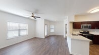 This single-story, 2-bedroom, 2-bathroom residence in Houston, TX offers a well-designed open-concept layout that maximizes functionality and comfort. The expansive living area is finished with rich, dark hardwood-style flooring and features a ceiling fan, while multiple windows fitted with blinds fill the space with natural light. The kitchen is a standout, equipped with stainless steel appliances including a gas range, microwave, and refrigerator, complemented by deep espresso-toned cabinetry, a tile backsplash, and a curved breakfast bar with a built-in sink that opens seamlessly to the living area. Both bedrooms are carpeted for warmth and comfort, each featuring ceiling fans and windows that allow ample natural light. The two bathrooms are finished with hardwood-style flooring and white cabinetry. One bathroom includes a vanity with a large mirror and lighted fixture alongside a tiled shower-tub combo, while the second features a clean, tiled tub-shower combination with chrome fixtures. Clean white walls and consistent flooring choices throughout lend the space a cohesive, modern aesthetic well-suited for comfortable everyday living.