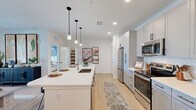Located at 1230 Front Pl in North Port, FL, this thoughtfully designed one-bedroom, one-bathroom unit offers a clean, modern aesthetic throughout its efficiently organized single-floor layout. The open-concept kitchen serves as the heart of the home, showcasing white shaker cabinetry, stainless steel appliances, herringbone tile backsplash, and a generous island with seating for multiple guests, illuminated by a trio of sleek pendant lights. Light wood-style flooring flows seamlessly throughout, enhancing the bright and airy atmosphere created by recessed lighting and natural light. The bedroom is a comfortable retreat featuring a ceiling fan, natural light from well-dressed windows, a soothing accent wall, and direct access to a dedicated closet. The full bathroom offers a dual-sink vanity with white countertops, framed mirrors, modern fixtures, and a full tub-shower combination with tile surround. A dedicated closet provides practical storage. The unit also includes a private, fenced outdoor green space — a rare and appealing feature that opens to views of the surrounding community. The overall design balances contemporary finishes with functional living, making this a well-rounded residential unit in a modern Florida community.