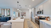 Located at 1230 Front Pl in North Port, FL, this thoughtfully designed one-bedroom, one-bathroom unit offers a clean, modern aesthetic throughout its efficiently organized single-floor layout. The open-concept kitchen serves as the heart of the home, showcasing white shaker cabinetry, stainless steel appliances, herringbone tile backsplash, and a generous island with seating for multiple guests, illuminated by a trio of sleek pendant lights. Light wood-style flooring flows seamlessly throughout, enhancing the bright and airy atmosphere created by recessed lighting and natural light. The bedroom is a comfortable retreat featuring a ceiling fan, natural light from well-dressed windows, a soothing accent wall, and direct access to a dedicated closet. The full bathroom offers a dual-sink vanity with white countertops, framed mirrors, modern fixtures, and a full tub-shower combination with tile surround. A dedicated closet provides practical storage. The unit also includes a private, fenced outdoor green space — a rare and appealing feature that opens to views of the surrounding community. The overall design balances contemporary finishes with functional living, making this a well-rounded residential unit in a modern Florida community.