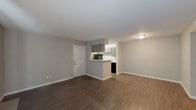 This single-floor residence offers a clean, functional layout designed for comfortable everyday living. The open-concept living area is anchored by rich, dark-toned hardwood-style flooring and neutral gray walls, creating a modern yet understated aesthetic. A large sliding glass door floods the living space with natural light, complemented by vertical blinds for privacy and light control.

The galley-style kitchen is efficiently designed with gray cabinetry, light countertops, and black appliances including an electric range, overhead exhaust hood, and refrigerator. A stainless steel sink and ample upper and lower cabinet storage round out this practical cooking space. A peninsula counter connects the kitchen to the living area, offering a convenient pass-through and casual dining option.

The bedroom is a comfortable retreat featuring plush carpeting, a ceiling fan with integrated lighting, and a window with blinds that allow for natural light. The full bathroom is finished in crisp white tones, featuring a tub and shower combination with a chrome curtain rod, a toilet, and coordinating fixtures. The flooring throughout transitions seamlessly between the hardwood-style surfaces in the main living areas and carpet in the bedroom, contributing to a cohesive and inviting overall atmosphere.