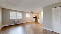 Located at 7155 Raleigh St in Westminster, CO, this single-floor, one-bedroom, two-bathroom unit offers a practical and well-organized layout. The open living area is finished with warm wood-look vinyl flooring, a textured ceiling, a ceiling fan, and a wall-mounted AC unit, complemented by a large window that draws in natural light and views of surrounding greenery. Baseboard heating runs throughout, providing efficient warmth. The kitchen flows directly off the living space and features white cabinetry, subway tile backsplash, dark countertops, stainless steel appliances including a refrigerator and range, and a double-basin sink — with an adjacent pantry offering additional storage. The bedroom is carpeted for comfort, includes a large double-door closet, and connects conveniently to one of the two bathrooms, which features a vanity with a dark countertop, under-sink cabinet, and wood-look flooring. A second bathroom and hallway closet add further functionality. The unit's neutral color palette of soft grays and warm beiges creates a clean, cohesive ambiance throughout, making it a straightforward and comfortable residential space.