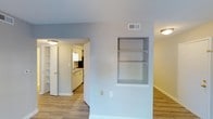 Located at 903 Kensington Dr in Cary, NC, this single-story home offers a clean, functional layout with a bright and welcoming atmosphere throughout. The main living area features light-toned hardwood-style flooring that flows seamlessly through the space, complemented by neutral wall tones and a textured ceiling that adds subtle character. A standout architectural detail is the built-in wall shelving unit, recessed neatly into the wall and ideal for displaying décor or storing everyday essentials. On the opposite side, additional built-in shelving provides further storage and display opportunities, enhancing the home's practical appeal. An open passageway connects the living area to the kitchen, which is outfitted with crisp white cabinetry, a sink positioned beneath a functional range hood, and ample counter space. The kitchen's bright, efficient design makes it well-suited for everyday cooking and meal preparation. Flush-mount ceiling lighting provides consistent illumination throughout, and ceiling vents indicate a central HVAC system for year-round comfort. The overall aesthetic is fresh, tidy, and move-in ready, making this Cary home an approachable and well-maintained residence.