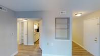 Located at 903 Kensington Dr in Cary, NC, this single-story home offers a clean, functional layout with a bright and welcoming atmosphere throughout. The main living area features light-toned hardwood-style flooring that flows seamlessly through the space, complemented by neutral wall tones and a textured ceiling that adds subtle character. A standout architectural detail is the built-in wall shelving unit, recessed neatly into the wall and ideal for displaying décor or storing everyday essentials. On the opposite side, additional built-in shelving provides further storage and display opportunities, enhancing the home's practical appeal. An open passageway connects the living area to the kitchen, which is outfitted with crisp white cabinetry, a sink positioned beneath a functional range hood, and ample counter space. The kitchen's bright, efficient design makes it well-suited for everyday cooking and meal preparation. Flush-mount ceiling lighting provides consistent illumination throughout, and ceiling vents indicate a central HVAC system for year-round comfort. The overall aesthetic is fresh, tidy, and move-in ready, making this Cary home an approachable and well-maintained residence.