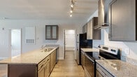 Located at 100 Comet Creek Ln in Goose Creek, SC, this single-floor residence offers a thoughtfully designed layout that maximizes comfort and functionality. The open-concept living and kitchen area serves as the heart of the home, where wood-look flooring flows seamlessly throughout. The kitchen is a standout feature, boasting granite countertops, a peninsula with an integrated sink, dark-toned cabinetry with frosted glass upper cabinets, stainless steel appliances including a refrigerator and electric range, and a sleek stainless steel wall-mounted range hood illuminated by stylish track lighting. The living area is bright and airy, anchored by elegant French doors with a transom window above, allowing natural light to pour in and providing outdoor access. The generously sized bedroom is finished with plush carpeting, a ceiling fan, and windows that offer natural light and views of the surrounding greenery. A spacious walk-in closet with wire shelving provides ample storage. The bathroom features wood-look tile flooring, a granite-topped vanity with dark cabinetry, and a full tub-shower combination, completing this clean and cohesive living space.