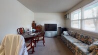 Located at 68 Parker St in Acton, MA, this single-floor unit offers a practical and well-organized layout across several distinct living areas. The kitchen is equipped with warm oak cabinetry, granite-look countertops, tile flooring, and a full suite of appliances including a coil-top electric range, making it a functional space for everyday cooking. Adjacent to the kitchen, the combined living and dining area provides a comfortable, carpeted space with a window that allows natural light to filter in, accommodating both a dining table set and a sitting area. The primary bedroom features carpeted flooring, a window dressed with patterned curtains, and a closet, offering a quiet and private retreat. A second bedroom is similarly carpeted and well-proportioned, providing flexibility for use as a guest room or sleeping quarters. An additional room with a window and carpeted flooring offers versatile potential, suitable as a home office or storage space. The full bathroom includes tile flooring, a vanity with wood cabinetry, a toilet, and a tub-shower combination with white tile surround, providing all essential amenities. The unit's neutral wall tones and consistent flooring materials throughout create a cohesive and understated interior atmosphere.