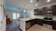 This single-floor residence offers a thoughtfully designed open-concept layout that seamlessly connects the kitchen, dining, and living areas. The kitchen is a standout feature, showcasing rich dark espresso cabinetry, granite countertops, a mosaic tile backsplash, and a full suite of stainless steel appliances including a range, microwave, dishwasher, and refrigerator. A peninsula with bar seating and pendant lighting above serves as both a functional workspace and a casual dining spot. The living area is bright and welcoming, with durable wood-look flooring, crown molding, and a ceiling fan. A set of double French doors floods the space with natural light and provides access to the outdoors. The bathroom features a double-sink vanity topped with granite, dark cabinetry, and a large mirror, offering ample counter space and storage. The bedrooms are carpeted for comfort, each equipped with ceiling fans and windows dressed with blinds that allow for natural light. The overall ambiance of this residence is clean, modern, and cohesive, with neutral tones and quality finishes carried consistently throughout each room.