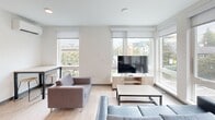 Located at 4759 15th Ave NE in Seattle's University District, this 2-bedroom, 1-bathroom unit offers a clean, contemporary design across a single floor. The open-concept kitchen and living area serves as the heart of the space, where light wood-style flooring and crisp white walls create a bright, cohesive atmosphere. The kitchen is well-appointed with stainless steel appliances — including a refrigerator, range, microwave, and dishwasher — complemented by light wood cabinetry, stone-look countertops, and a blue-gray tile backsplash that adds a subtle pop of color. The living room is bathed in natural light from expansive windows that frame views of the surrounding urban neighborhood. Both bedrooms are efficiently laid out, each featuring light-filled windows, ceiling fans, and built-in closet space. The primary bedroom offers a comfortable footprint suited for a bed and additional furnishings. The shared bathroom features a single-sink vanity with light wood cabinetry, a white countertop, and a large mirror. Throughout the unit, consistent light wood flooring and neutral tones provide a modern, functional living environment well-suited to the vibrant University District location.