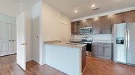 This single-story residence offers a thoughtfully designed layout across two bedrooms and two bathrooms, making efficient use of its compact footprint. Warm wood-look flooring runs consistently throughout the unit, providing a cohesive aesthetic that ties each room together.

The kitchen serves as a functional centerpiece, featuring rich dark-toned cabinetry with glass-front upper cabinets, light granite countertops, and a full suite of stainless steel appliances including a range, microwave, and refrigerator. A peninsula with an integrated sink and additional counter space extends toward the living area, creating an open, connected feel between the kitchen and living room.

The living room is bright and airy, benefiting from a ceiling fan and a window that allows natural light to filter in. Both bedrooms are well-proportioned, with the primary bedroom offering a comfortable, generously sized retreat. The bathrooms are clean and functional, each featuring a tub/shower combination and matching wood-look flooring. A hallway connects the rooms efficiently, and a dedicated closet provides additional storage. The unit's neutral white walls and recessed lighting create a clean, modern ambiance throughout.