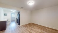 Located at 1210 NW 13th St in Boca Raton, Florida, this single-floor unit features a clean, updated interior designed for comfortable everyday living. Light wood-tone laminate flooring runs throughout the main living areas and bedrooms, lending a warm, cohesive feel to the space. The open layout connects the living area directly to the kitchen, which is outfitted with rich, dark wood cabinetry, light quartz countertops, a white tile mosaic backsplash, stainless steel sink with pull-out faucet, black appliances including a range and refrigerator, and an over-the-range microwave. The bedroom offers natural light through a window with blinds and includes a reach-in closet with a rod and shelving. An additional room provides flexible use as a second bedroom or living space, also with natural light and neutral walls. The bathroom features full floor-to-ceiling tile surrounding a soaking tub and shower combination, complemented by a quartz vanity countertop and dark wood cabinetry. Throughout the unit, white walls and trim create a bright, neutral backdrop, while flush-mount lighting provides consistent illumination across all rooms.
