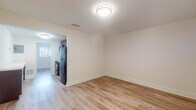 Located at 1210 NW 13th St in Boca Raton, Florida, this single-floor unit features a clean, updated interior designed for comfortable everyday living. Light wood-tone laminate flooring runs throughout the main living areas and bedrooms, lending a warm, cohesive feel to the space. The open layout connects the living area directly to the kitchen, which is outfitted with rich, dark wood cabinetry, light quartz countertops, a white tile mosaic backsplash, stainless steel sink with pull-out faucet, black appliances including a range and refrigerator, and an over-the-range microwave. The bedroom offers natural light through a window with blinds and includes a reach-in closet with a rod and shelving. An additional room provides flexible use as a second bedroom or living space, also with natural light and neutral walls. The bathroom features full floor-to-ceiling tile surrounding a soaking tub and shower combination, complemented by a quartz vanity countertop and dark wood cabinetry. Throughout the unit, white walls and trim create a bright, neutral backdrop, while flush-mount lighting provides consistent illumination across all rooms.
