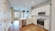 Located in the heart of Colorado Springs at 410 E Pikes Peak Ave, this well-appointed one-bedroom, one-bathroom residence offers a thoughtfully designed layout across a single floor. The open-concept kitchen is a standout feature, showcasing crisp white shaker cabinetry, a classic subway tile backsplash, light quartz countertops, and a full suite of stainless steel appliances including a refrigerator, range, microwave, and dishwasher. Stylish black pendant lights hang over the kitchen peninsula, which flows seamlessly into the living area. The living room is bathed in natural light through large windows and a glass door, offering urban views of the Colorado Springs skyline, and is finished with warm hardwood-style flooring and a ceiling fan. The bedroom features plush carpet, a generous window framing city and mountain views, and direct access to a well-organized walk-in closet with built-in shelving and double hanging rods. The bathroom is finished with large-format tile flooring and a glass-enclosed walk-in shower with subway tile surround. The entrance area includes a functional built-in mudroom bench with overhead cabinetry, providing practical storage. Neutral tones throughout lend the space a clean, modern ambiance.