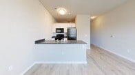 This efficiently designed studio unit in Greeley, Colorado offers a thoughtful single-floor layout that maximizes every square foot. The open-concept living and kitchen area is anchored by a peninsula-style counter with a dark laminate surface and double sink, providing both workspace and a natural divider between the living space and kitchen. White cabinetry lines the kitchen walls, complemented by black appliances including a refrigerator, range, and over-the-range microwave. Light wood-style luxury vinyl flooring runs throughout the main living areas, lending a clean and contemporary feel.

The bedroom is a private, carpeted retreat with neutral warm-toned walls and ample outlet access, offering a comfortable and quiet space. An adjoining closet provides dedicated storage. Ceiling fans are present in both the living and bedroom areas, promoting year-round comfort.

The bathroom features light wood-style flooring consistent with the rest of the unit, a white vanity with dark countertop, a large mirror with overhead lighting, a standard soaking tub with shower, and a towel bar — all presented in a clean, functional layout. The unit's neutral color palette and modern finishes throughout create a cohesive, move-in-ready atmosphere suitable for everyday living.