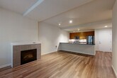 Located in Seattle, WA, this well-appointed 1-bedroom, 2-bathroom residence offers a thoughtfully designed single-level layout. The open-concept living and kitchen area serves as the heart of the home, featuring warm hardwood flooring, track lighting, and a tile-surround fireplace that anchors the living space. Large windows and a glass patio door flood the area with natural light and frame pleasant views of surrounding trees.

The kitchen is outfitted with rich wood cabinetry, dark granite countertops, a stainless steel appliance suite including a gas range, microwave, and refrigerator, and a peninsula with an integrated sink — ideal for both cooking and casual dining.

The bedroom is carpeted for comfort and includes generous closet space with additional closets found throughout the unit. A large window provides natural light and treetop views, creating a serene retreat. The bathrooms are finished with tile flooring and warm wood vanities with dark countertops; one bathroom conveniently houses an in-unit stacked washer and dryer. A private patio extends the living space outdoors, completing this efficient and comfortable Seattle residence.