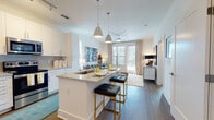 Located at 4011 Tryon Park Rd in Charlotte, NC, this single-floor residence offers a thoughtfully designed open-concept layout with modern finishes throughout. The kitchen serves as a central hub, featuring white shaker cabinetry, granite countertops, a subway tile backsplash, stainless steel appliances, and a large island with seating — ideal for both everyday meals and entertaining. Pendant lighting above the island adds a stylish touch, while wood-style flooring extends seamlessly into the living and dining areas. The living room is bright and welcoming, with large windows and a glass-paneled door that invite abundant natural light and provide access to an outdoor balcony. The bedroom is a comfortable retreat, highlighted by generous window coverage, warm ambient lighting, and direct access to a spacious walk-in closet outfitted with wire shelving and ample hanging and storage space. The en-suite bathroom offers a dual-sink vanity with granite countertops, white cabinetry, a glass-enclosed shower, and wood-style flooring that carries the home's cohesive aesthetic throughout. Clean white walls, contemporary fixtures, and a neutral color palette give the entire space a polished, move-in-ready feel.