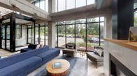 Located at 1367 Willow Street in Minneapolis, Minnesota, this contemporary lobby space makes a striking first impression through its bold industrial-modern design. Exposed concrete columns and beams rise dramatically overhead, framing expansive floor-to-ceiling windows that flood the interior with abundant natural light and offer open views of the surrounding greenery and streetscape.

The main lounge area anchors the space with a generous sectional sofa in deep navy blue, complemented by tufted gray accent chairs and a central fireplace, creating a welcoming and sophisticated gathering environment. Light wood-plank flooring runs throughout, softening the industrial concrete aesthetic and adding warmth.

A secondary seating area features tall, curved wingback chairs in slate blue with vibrant yellow accent pillows, arranged around natural wood side tables. Warm-toned wood cladding on structural columns and partition walls introduces an organic richness that contrasts beautifully with the building's raw concrete framework.

The entrance is highlighted by a bold, large-scale abstract mural in teal, yellow, and blush tones, positioned beneath a sleek open-riser staircase with glass railings — a true focal point that adds artistic character to the space. Together, these elements create a polished, inviting environment that balances urban industrial architecture with comfortable, thoughtfully curated design.