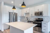 Located at 221 Rustic Point Ln in Madison, WI, this thoughtfully designed one-bedroom, three-bathroom unit offers a clean, modern aesthetic throughout. The open-concept living and kitchen area is anchored by light wood-tone flooring, crisp white walls, and abundant natural light from large windows and sliding glass doors that lead to a private balcony with outdoor views.

The kitchen is a standout feature, boasting white shaker cabinetry, a classic white subway tile backsplash, quartz countertops, a center island with pendant lighting, and a full suite of stainless steel appliances including a refrigerator, range, microwave, and dishwasher. A stacked washer and dryer unit is conveniently integrated nearby.

The bedroom is carpeted for comfort, fitted with a ceiling fan, and receives generous natural light through large windows. The three bathrooms are finished with quartz vanity tops, white cabinetry, and sleek matte black fixtures, lending a contemporary contrast to the bright, neutral palette. One bathroom features a soaking tub with matching black hardware.

Throughout the unit, matte black accents on hardware and fixtures provide a cohesive modern touch, while recessed lighting and pendant lights ensure a well-lit, welcoming ambiance across all spaces.