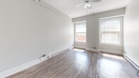 Located at 50 Franklin St in Worcester, MA, this single-floor unit offers a clean, functional layout suited for a variety of uses. The main living areas feature durable hardwood-style flooring in a neutral gray-toned finish, complemented by soft gray walls that create a bright and airy atmosphere. Multiple windows allow natural light to flow throughout, offering views of the surrounding urban streetscape. A ceiling fan with a light fixture serves the primary room, which also includes track lighting along the ceiling and baseboard heating for year-round comfort. The kitchen is equipped with dark cabinetry offering ample storage, granite-style countertops, a stainless steel refrigerator, a utility sink, and a white square-tile backsplash, all set on classic tile flooring. The bathroom continues the tile flooring aesthetic with warm-toned tiles underfoot, a dark-cabinet vanity with a lit mirror, a toilet, towel bars, and a tiled shower area. The overall design is practical and understated, with consistent neutral tones throughout. The unit's straightforward, open layout and well-maintained finishes make it a versatile space in the heart of Worcester.