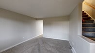 Located at 1524 Regent Ave in Springfield, Ohio, this three-floor home provides a well-distributed layout across its main level, upper floor, and basement. The main level features a carpeted living area with neutral gray-toned walls, a staircase, and a front entry with a glass-paneled door and a large window that allows natural light and exterior views. Adjacent to the entry is a kitchen equipped with white shaker-style cabinetry, black hardware, light stone-patterned countertops, a double-basin sink, and wood-look vinyl flooring, offering a clean, updated aesthetic.

The upper level contains multiple carpeted bedrooms with neutral walls and white baseboards. One bedroom features a walk-in closet with a clothing rod, accessible through a warm wood-toned door. A full bathroom on this level includes a shower-tub combination with white surround panels, chrome fixtures, a window for natural light, and a toilet. The rooms are well-proportioned, providing comfortable living space throughout.

The basement level offers an unfinished utility and storage space with painted concrete block walls, a sealed gray floor, a small window, and exposed overhead infrastructure, making it suitable for storage or future development.