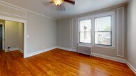 Located in the sought-after neighborhood of Washington, DC, this single-floor unit at 3621 Newark St NW offers a well-appointed layout with timeless character. Warm hardwood floors extend throughout the living areas and bedrooms, creating a cohesive and inviting atmosphere. The living spaces are generously proportioned, with crown molding, classic white trim, and ceiling fans adding to the traditional aesthetic. Natural light filters in through multiple windows fitted with blinds, offering pleasant views of the surrounding neighborhood. A classic cast-iron radiator provides supplemental heating in select rooms, complementing the vintage charm of the space. The galley-style kitchen is efficiently designed, featuring rich dark wood cabinetry, granite-style countertops, stainless steel appliances including a refrigerator, and a window that brings in natural light. The bathroom presents a clean, bright finish with white subway tile walling, tile flooring, a pedestal sink, a bathtub, and a window overlooking greenery. Bedrooms are well-sized with neutral wall tones and include features such as closets and ceiling fans. An entry foyer with hardwood flooring and a solid door provides a welcoming transition into the home. This unit combines classic Washington, DC architectural details with functional, comfortable living spaces.