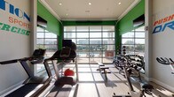 Located at 1809 Meeting St in Lexington, Kentucky, this fitness center is a thoughtfully designed, single-floor facility built to support a comprehensive workout experience. The space is defined by a bold, energetic aesthetic — vibrant green accent walls contrast with light-toned wood-style flooring, while motivational fitness-themed typography covers the walls, featuring words like "Dream," "Believe," "Committed," and "Determination."

A standout architectural feature is the full-height glass garage door wall that floods the interior with natural light and offers direct views of an outdoor pool area, creating an open, airy atmosphere. Recessed ceiling lighting and a ceiling fan supplement the abundant natural light throughout.

The gym is comprehensively equipped for a variety of training styles. Cardio equipment includes treadmills, elliptical machines, and stationary bikes, all positioned to take advantage of the poolside views. A dedicated free weights section features a full rack of dumbbells, kettlebells, and medicine balls, alongside a weight bench and spin bike. Stability equipment such as balance balls and ball chairs adds functional training options. Large wall mirrors expand the sense of space and support proper form during workouts. Wall-mounted televisions are positioned throughout for entertainment during exercise sessions.