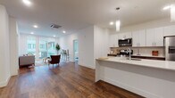 This well-designed single-floor residence combines modern aesthetics with practical living. Rich hardwood flooring flows throughout the open-concept main area, connecting the kitchen, dining, and living spaces seamlessly. The kitchen is a standout feature, showcasing crisp white upper cabinetry paired with dark lower cabinets, a bold quartz peninsula with an undermount sink, stainless steel appliances including a gas range, microwave, and refrigerator, and elegant pendant lighting overhead. The open layout transitions naturally into the living area, which is bathed in natural light from floor-to-ceiling sliding glass doors that open to a private balcony with views of the surrounding building community. The bedroom continues the hardwood flooring and features its own sliding glass door access to an outdoor balcony, filling the room with abundant natural light. The bathroom is finished with wood-look tile flooring, a tiled shower-tub combination with distinctive vertical wood-grain tile surround, and a clean white floating vanity. Completing the unit is a dedicated in-unit laundry space equipped with a stacked Whirlpool washer and dryer. Recessed lighting throughout and crisp white walls contribute to the bright, contemporary ambiance of this thoughtfully appointed residence.