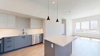 Located in the heart of Hollywood at 1233 N Highland Ave, this modern 2-bedroom, 2-bathroom unit offers a thoughtfully designed open-concept layout with contemporary finishes throughout. Light hardwood flooring flows seamlessly across the entire space, complementing the bright, neutral palette and soaring ceilings that lend an airy, expansive feel.

The combined kitchen and living area serves as the centerpiece of the unit. The kitchen is outfitted with dual-tone cabinetry — white upper cabinets paired with slate-blue lowers — a quartz waterfall island with pendant lighting, stainless steel appliances including a French door refrigerator, and a marble-style tile backsplash. The open living area provides generous space for entertaining.

Both bedrooms are well-proportioned and filled with natural light. The primary bedroom offers ample space and is served by a sleek en-suite bathroom featuring a large-format dark tile walk-in shower, a backlit vanity mirror, and a blue-grey double vanity with quartz countertop. The second bathroom includes a soaking tub with dark tile surround and a window for natural light.

Additional highlights include three closets, a dedicated in-unit laundry area, and city and treetop views from multiple windows showcasing the Los Angeles skyline.