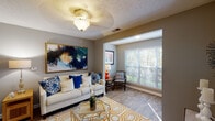 This single-floor residence offers a thoughtfully designed layout that balances comfort and functionality across its key living spaces. The living room serves as the heart of the home, featuring wood-look flooring, a ceiling fan with light fixture, and a sunlit reading nook with large windows that invite natural light and outdoor views. Neutral gray walls provide a versatile backdrop throughout the space.

The kitchen is outfitted with crisp white cabinetry, dark countertops, and stainless steel appliances including a refrigerator, range, and microwave. A peninsula-style counter separates the kitchen from the open dining area, which accommodates a round glass-top table beneath a pendant light fixture. The kitchen also features wood-look flooring that carries through from the main living areas.

Two well-proportioned bedrooms offer carpeted flooring and ceiling fans, each with windows providing natural light. The primary bedroom features a textured ceiling and ample space for a queen or king bed. Two bathrooms serve the residence — one with a tub-shower combination, wood-look flooring, and a vanity with white cabinetry, and a second full bathroom also featuring a tub-shower with decorative accents and wood-look flooring. The overall ambiance is warm, cohesive, and move-in ready.
