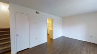 This multi-floor property spans three levels and offers a clean, well-maintained interior designed for comfortable everyday living. The main living area is an open, bright space featuring rich dark hardwood-style flooring that contrasts beautifully with the crisp white walls, creating a warm yet modern aesthetic. A textured ceiling adds a classic touch to the room, while a ceiling-mounted HVAC vent ensures year-round climate control. The living space flows naturally into the kitchen, which is visible through a wide doorway and features lighter flooring, white cabinetry, and full-size appliances including a refrigerator. The kitchen layout appears functional and compact, providing efficient use of the available space. Throughout the property, the white walls and neutral finishes create a versatile backdrop that adapts easily to a variety of interior styles. The overall ambiance is clean and practical, with a straightforward design that emphasizes usability. Spread across three floors, the property offers ample separation of living spaces, providing both communal areas and private zones suited to a range of occupants.