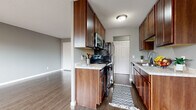This single-floor residence offers a cohesive and practical layout designed for comfortable everyday living. The galley-style kitchen is a standout feature, showcasing rich warm-toned wood cabinetry that extends to the ceiling for generous storage capacity. Light granite-style countertops provide ample prep space, while stainless steel appliances—including a gas range, built-in microwave, and refrigerator—complete the functional setup. Dark hardwood-style flooring runs throughout, tying the kitchen seamlessly into the adjacent open living area. The living space is bright and open, with neutral gray walls and a large closet offering additional storage. Natural light filters in from multiple windows, contributing to an airy atmosphere. The bedroom continues the consistent flooring and gray color palette, featuring two windows that allow for cross ventilation and views of the surrounding neighborhood, along with a baseboard heating unit. The bathroom is well-equipped with a wood-toned vanity, a tub-shower combination, and coordinated fixtures. A textured ceiling treatment is present throughout the unit, adding a subtle design detail. Overall, the space presents a clean, neutral aesthetic with warm wood accents and durable finishes suited for practical, everyday living.