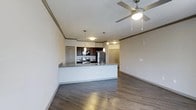 This single-floor residence showcases an open-concept layout that seamlessly connects the kitchen and living areas, creating a cohesive and functional living space. The kitchen is outfitted with stainless steel appliances, including a refrigerator and electric range, complemented by dark espresso cabinetry and granite countertops. A peninsula with a built-in sink extends into the space, providing additional prep area and casual seating potential. Pendant lighting hangs above the peninsula, adding focused illumination and a contemporary design touch.

The living area benefits from a ceiling fan with integrated lighting, promoting airflow and comfort throughout the space. Crown molding lines the upper walls, lending an elevated, polished aesthetic to the interior. Rich, dark hardwood-style flooring runs throughout, grounding the space with warmth and visual continuity. Neutral-toned walls enhance the brightness of the space, while raised panel doors lead to additional rooms beyond. The overall design balances modern finishes with classic architectural details, resulting in a refined and welcoming atmosphere.