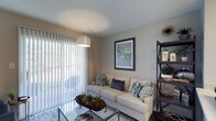 Located at 4075 Alkire Glen Way in Columbus, Ohio, this single-floor residence offers a comfortable and well-appointed living environment designed with both function and style in mind. The living area serves as the heart of the home, characterized by neutral wall tones that create a calm, inviting atmosphere. A large sliding glass door fitted with vertical blinds allows generous natural light to fill the space while providing convenient access to the outdoors. The room accommodates a generous seating arrangement centered around a glass-top coffee table, making it well-suited for both relaxing and entertaining. Decorative touches, including framed wall art, an open shelving unit, and thoughtfully placed accent pieces, contribute to the space's modern and curated aesthetic. The light-colored flooring is complemented by an area rug, adding warmth and texture underfoot. The overall design palette — featuring soft beiges, cool grays, and muted blues — lends a cohesive and contemporary feel throughout. The single-floor layout offers ease of navigation and accessibility, making this residence a practical and stylish option in the Columbus, OH area.