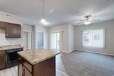 Located in Johnston, Iowa, this single-floor, 2-bedroom, 2-bathroom residence offers a well-organized layout designed for comfortable everyday living. The open-concept great room seamlessly connects the kitchen, dining, and living areas, creating a spacious and functional hub. The kitchen is outfitted with rich dark-wood cabinetry, granite-style countertops, black appliances including a range, microwave, refrigerator, and dishwasher, and a central island that provides additional prep space and casual seating. Light-toned hardwood-style flooring runs through the kitchen and living area, transitioning to plush carpet in the living room and bedrooms. A ceiling fan with light fixture anchors the living space, which opens to a private balcony through sliding glass doors, allowing for natural light and outdoor access. Both bedrooms are carpeted and feature vertical blind-covered windows. The bathrooms include dark vanity cabinetry with granite-style counters and tile flooring, with at least one bathroom offering a full tub-shower combination. Additional highlights include a dedicated laundry room with tile flooring, a utility room, and five closets distributed throughout the residence for ample storage.
