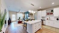 Located at 14300 Boggy Creek Rd in Orlando, FL, this single-floor, 2-bedroom, 2-bathroom residence offers a thoughtfully designed open-concept layout. The living room makes a strong first impression with a bold teal accent wall, ceiling fan, large windows that invite natural light, and warm wood-look flooring that flows seamlessly throughout the main living areas. The kitchen is a standout feature, boasting crisp white shaker cabinetry, white quartz countertops, a hex tile backsplash, stainless steel appliances, an undermount sink, open shelving, and a central island with pendant lighting and bar seating — all opening directly to the living area for effortless entertaining. The primary bedroom offers a comfortable retreat with plush carpet, natural light from dual windows, and direct access to the adjacent living space. The second bedroom is equally well-appointed. Both bathrooms are finished with white vanities, wood-look flooring, and clean, modern fixtures; one features a tiled soaking tub/shower combo. Each bedroom is complemented by a dedicated closet. The overall ambiance is modern and inviting, with a consistent neutral palette accented by thoughtful design details throughout.