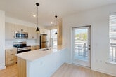 Located in Richmond, VA, this well-designed 1-bedroom, 2-bathroom unit offers a thoughtful layout across a single floor. The open-concept kitchen and living area serves as the heart of the space, featuring a large quartz-topped island with an undermount sink, pendant lighting, stainless steel appliances including a refrigerator and range, white subway tile backsplash, and a combination of warm wood lower cabinets and light upper cabinetry. A glass-paneled door provides direct outdoor access, filling the space with natural light. Light wood-tone luxury vinyl flooring flows seamlessly throughout. The living area is generously proportioned, with multiple large windows offering views of the surrounding neighborhood. The bedroom is a bright, comfortable retreat with its own windows and access to a spacious walk-in closet with wire shelving. An additional closet provides further storage. Both bathrooms are finished with clean white tile, warm wood vanities, quartz countertops, and black hardware accents. The primary bathroom features a double-sink vanity and a tiled walk-in shower. A connecting hallway ties the layout together efficiently. The overall aesthetic is clean, modern, and move-in ready, with consistent finishes and abundant natural light throughout.