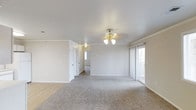 This single-story space presents a clean, neutral aesthetic throughout its open layout. The main living area is generously sized, finished with plush wall-to-wall carpeting in a warm gray tone that transitions to smooth hard flooring toward the hallway. Crown molding runs along the perimeter of the ceiling, adding a refined architectural detail to the otherwise minimalist design. A classic chandelier anchors the living space, providing both ambient lighting and a subtle decorative focal point.

Natural light filters in through a large sliding glass door along one wall, offering easy access to the outdoors while brightening the interior. The walls are painted in a soft, neutral tone that complements the light-colored finishes throughout.

A hallway leads to additional rooms, lined with multiple closet doors that suggest generous built-in storage. A window at the end of the corridor draws in additional natural light, keeping the passage bright and welcoming. Overall, the space maintains a fresh, move-in-ready feel with its clean lines, neutral palette, and practical layout suited to a variety of living arrangements.