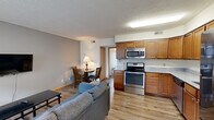 Located at 705 S First St in Champaign, Illinois, this single-floor unit offers a practical and well-appointed layout suited for comfortable everyday living. The open-concept living and dining area flows directly into the kitchen, creating a connected, functional space. Light gray walls and light wood-tone flooring run throughout the main living area, lending a clean and cohesive aesthetic. The living area is anchored by a wall-mounted flat-screen TV, a sofa, and a small dining table with chairs, making efficient use of the available space.

The kitchen is well-equipped with warm-toned wood cabinetry extending to the upper walls, granite-patterned countertops, and a full suite of stainless steel appliances, including an LG French door refrigerator, electric range, over-the-range microwave, and dishwasher. The kitchen's L-shaped layout maximizes counter and storage space.

The bedroom features carpeted flooring and floor-to-ceiling sliding glass doors with vertical blinds, providing access to an outdoor balcony and bringing in natural light with views of the surrounding Champaign streetscape. The full bathroom includes a white vanity with a single sink, an oval wall mirror, and a shower-tub combo with a curtain.